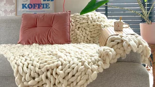 Een deken van lontwol in een creme kleur, over de bank, met een blokjespatroon gebreid.