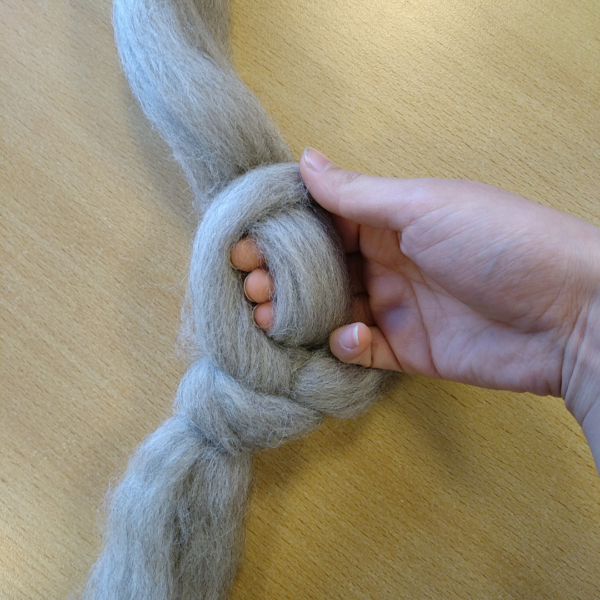 Close up van een hand die een streng lontwol breit door een lus te maken.