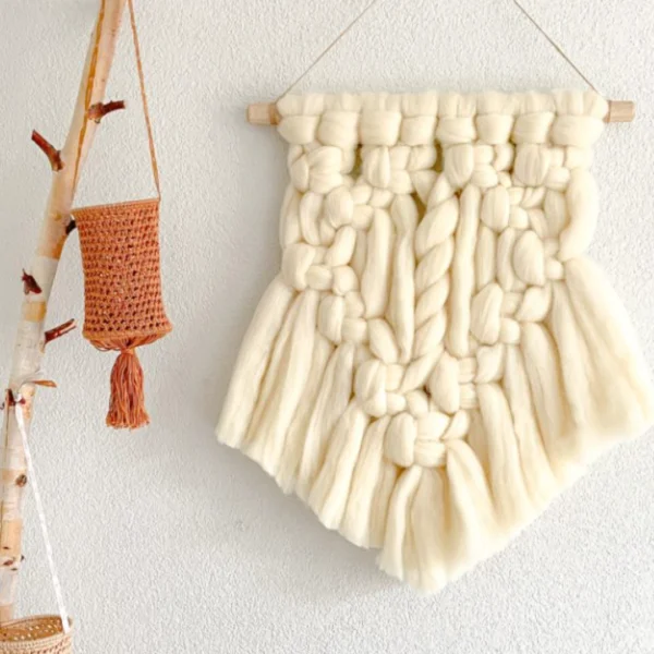 DIY macramé wandhanger van lontwol aan de muur naast een tak en een lampion.