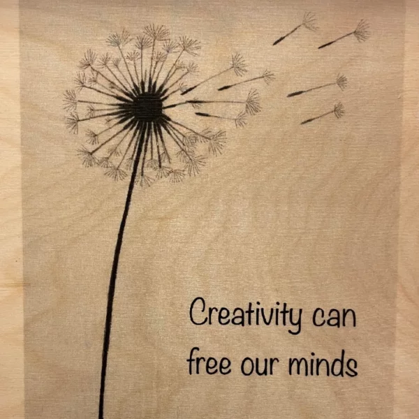 Uitgebloeide paardenbloem die weg waait op hout geprint met de tekst Creativity can free our minds.
