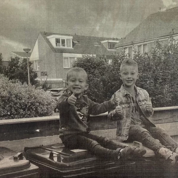 Zwart wit foto van 2 jongetjes buiten zittend op de vuilnisbak met hun duim omhoog geprint op hout als DIY.
