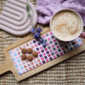 Borrelplank van hout met een mozaïek steentjes in paars, roze tinten met een kop chocolademelk en pepernoten.
