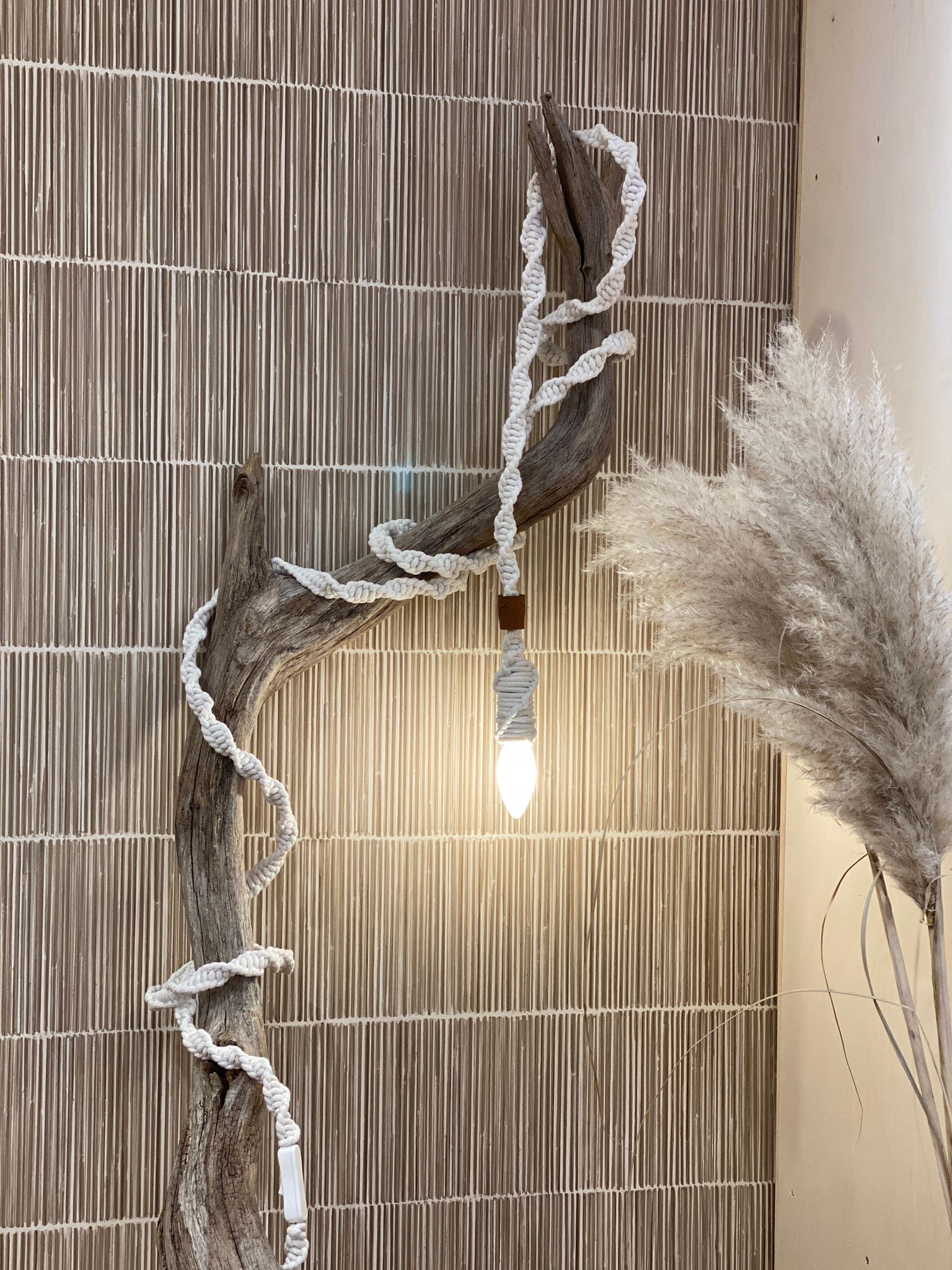 Lamp koord geknoopt met wit bobbiny garen in een bohemian stijl gefotografeerd met pluimen, een tak en riet behang.