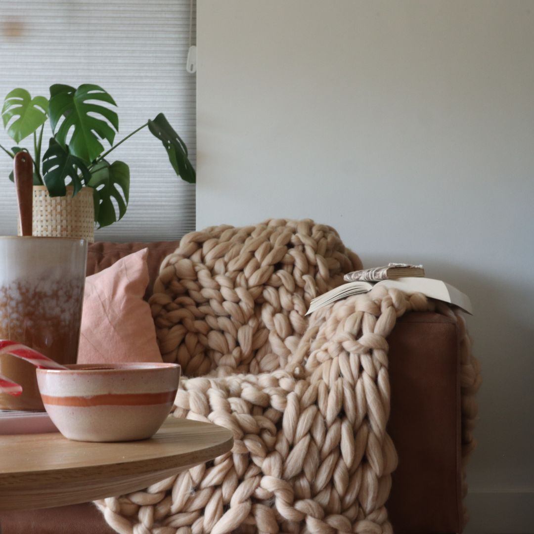 Zandkleurige deken gedrapeerd over een bruine bank met een koffie tafel en plant in de woonkamer.