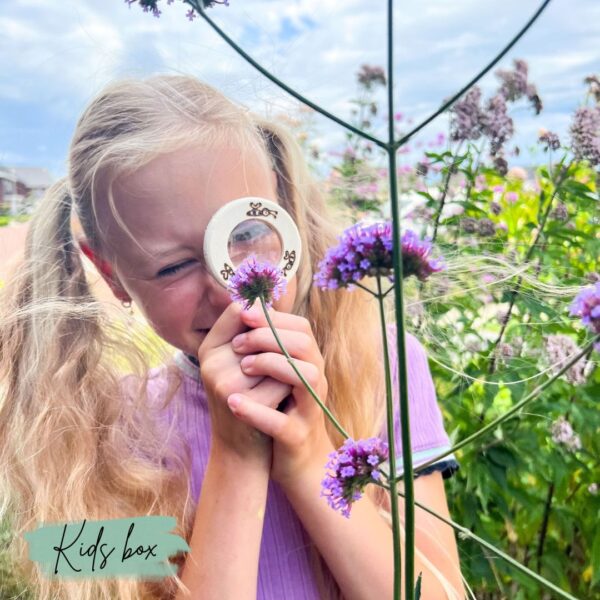 Een meisje kijkt door haar vergrootglas naar een grote paarse bloem in de bloementuin.