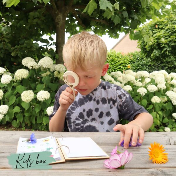 Jongetje zit aan de picknicktafel met zijn vergrootglas bloemen te bestuderen voor zijn notitieboekje.