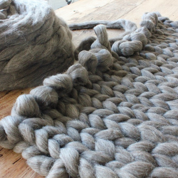 Woondeken van dikke wol die wordt geknoopt op tafel.