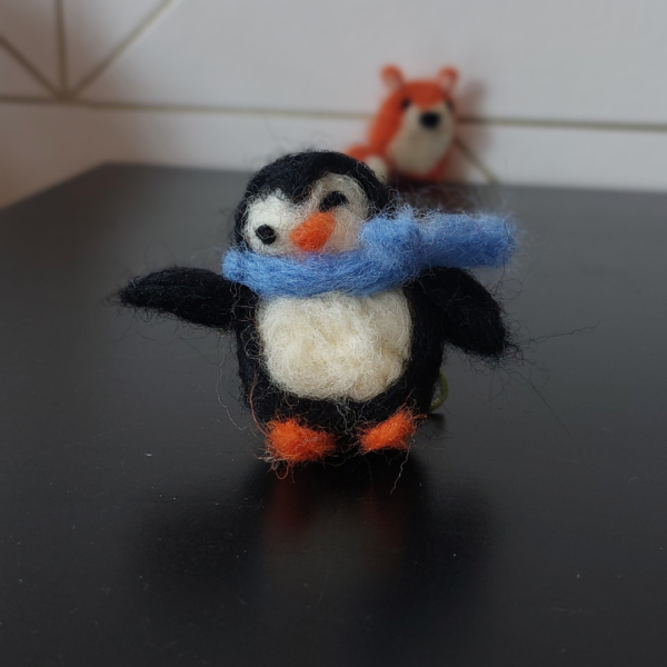 Pinguin van zwarte, blauwe, ivoorkleurige en oranje lontwol gemaakt met ons DIY pakket en tutorials.