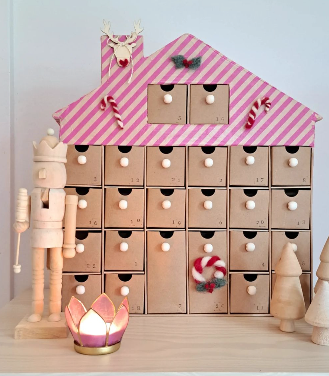 Adventhuis geknusteld met roze gestreept dak, en houten kerst figuren ervoor met een brandend kaarsje.