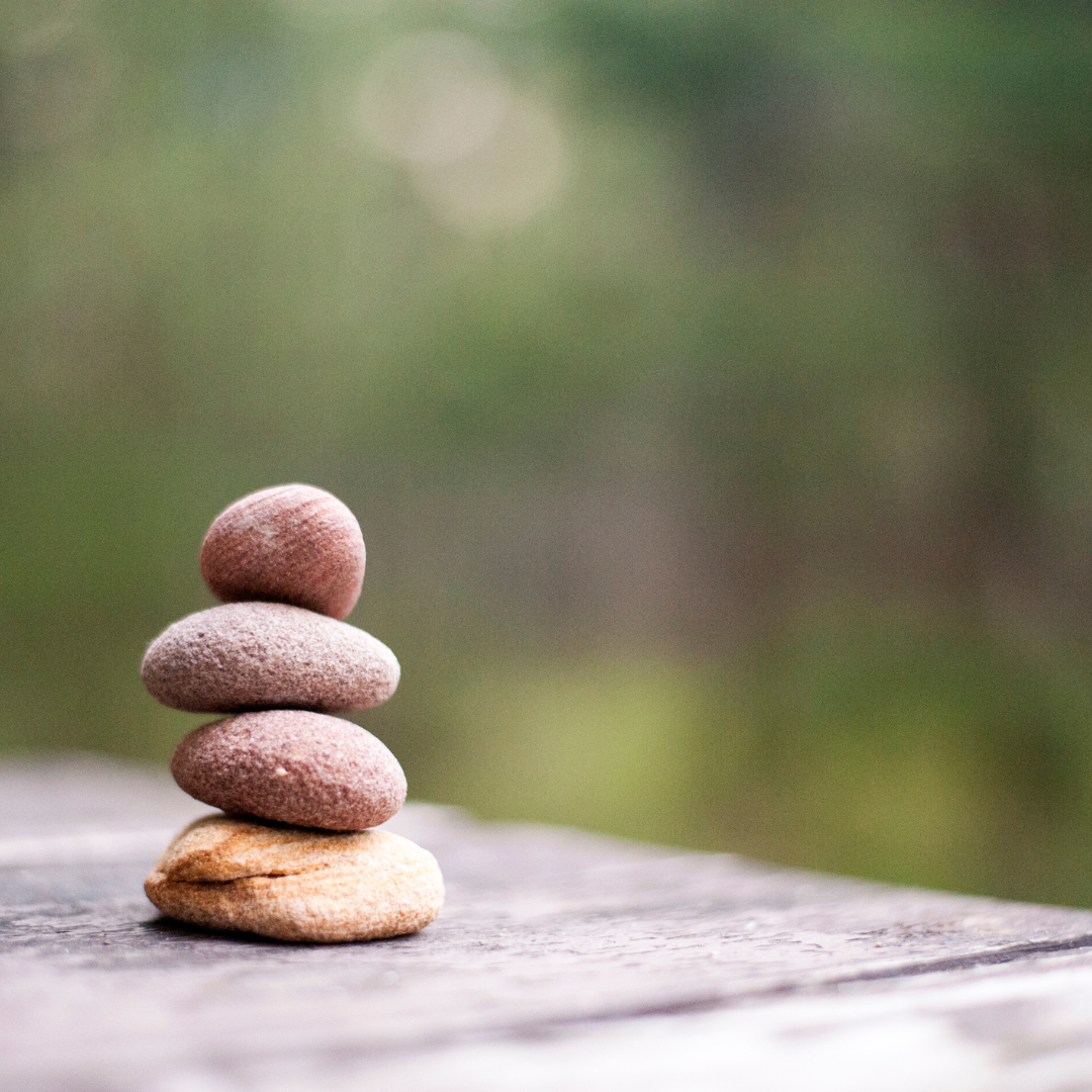 4 stenen op elkaar gestapeld in de natuur als voorbeeld van balans.