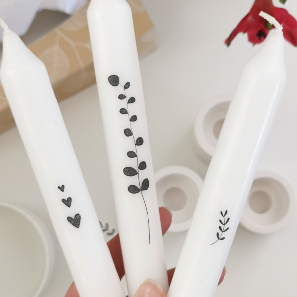 3 witte lange kaarsen versierd met zwarte stickers in hartjes, bloemen en teksten.