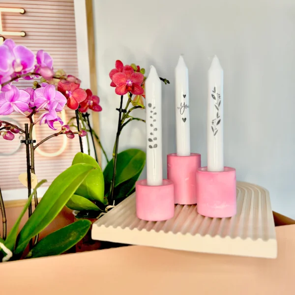Drie DIY kaarsenhouders gegoten met Raysin poeder in een roze tint, op een dienblad naast bloemen gevuld met witte kaarsen.
