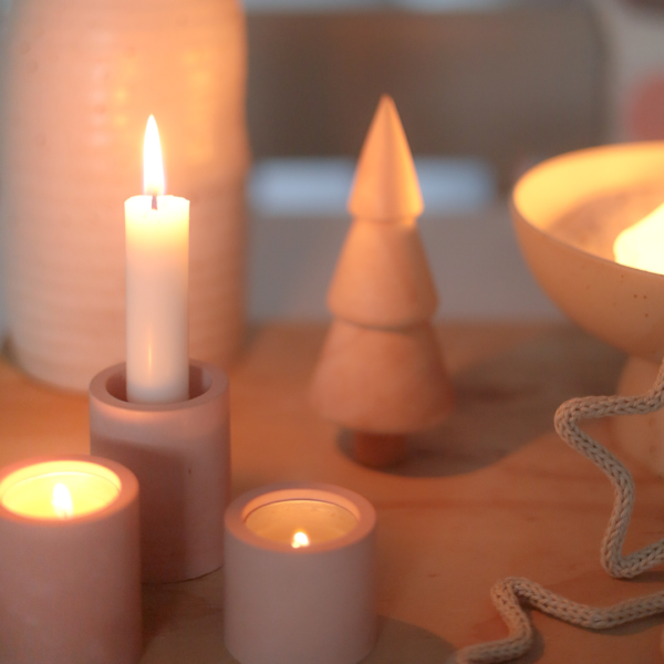 Brandende kaarsen en waxinelichtjes in lichtroze kaarsenhouders en een schaal op tafel.