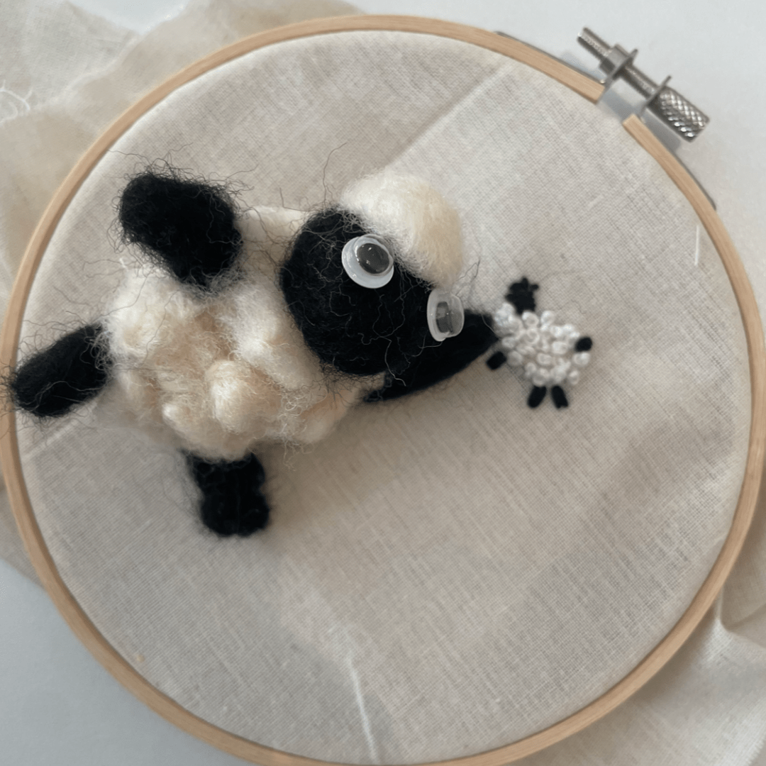 Shaun the Sheep prikvilten op een borduurring met een geborduurd schaapje.