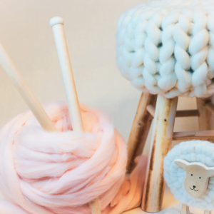 Lichtroze lontwol met dikke XXL houten breipennen, een gebreid krukje en houten schaapje.