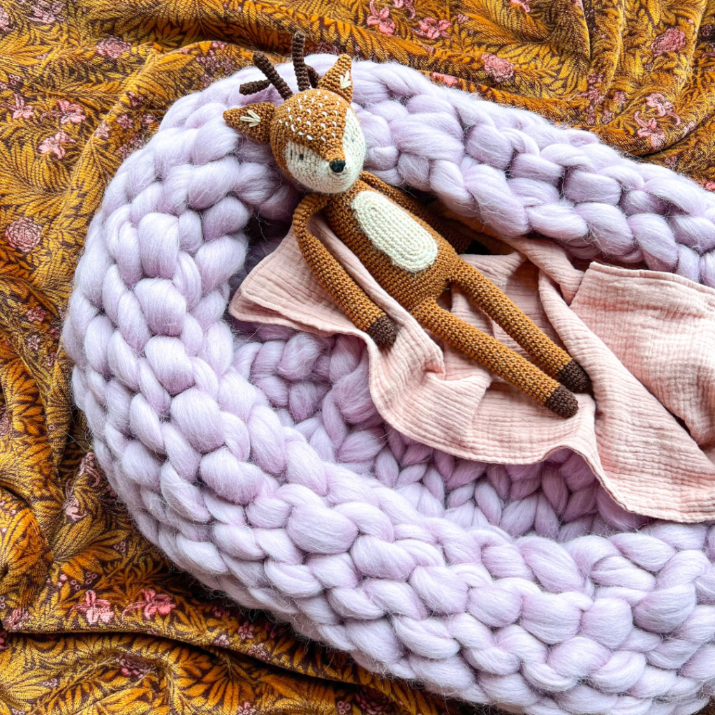 Babykrib van lila roze lontwol gebreid met een knuffel en deken erin.