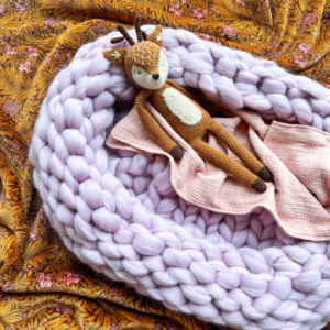 Babykrib van lila roze lontwol gebreid met een knuffel en deken erin.