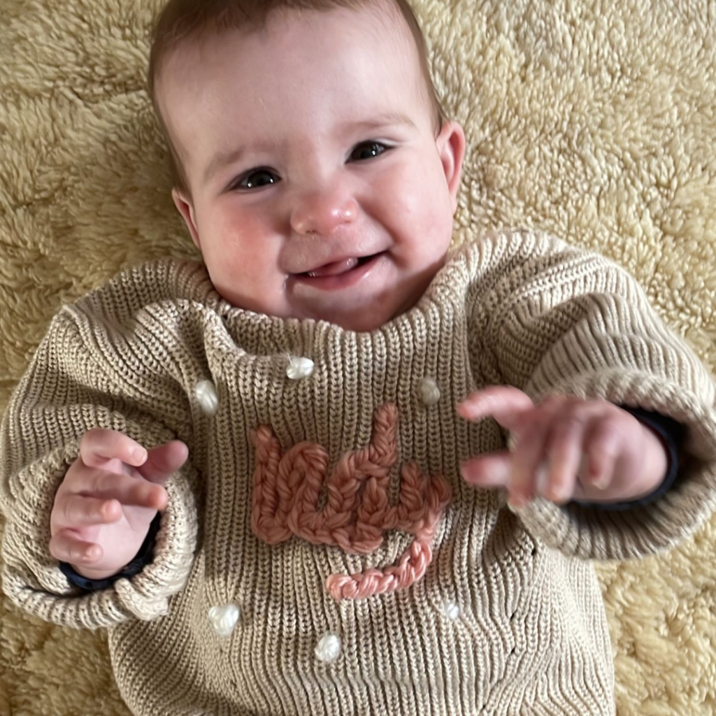 Indy (7 maanden) op een vachtje van wol met haar geborduurde trui met de naam Indy erop in kettingsteek.