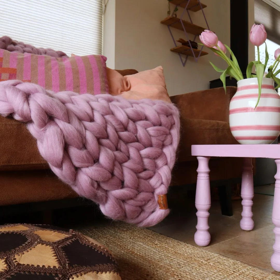 Lontwol deken blush op de bank met een roze tafeltje en bloemen.