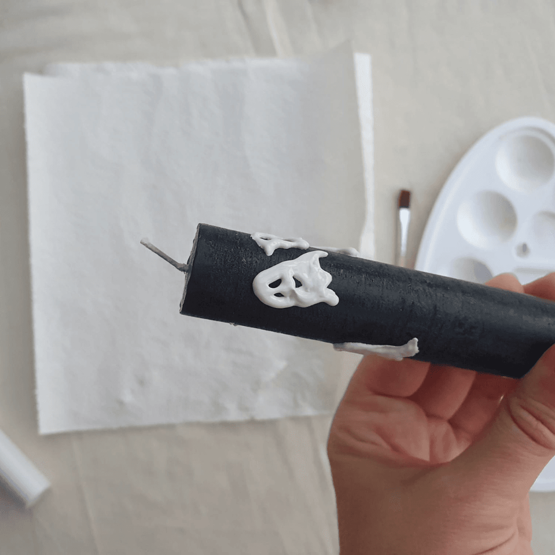 Maak spooky Halloween kaarsen met witte kaarsen stiften op zwarte kaarsen.