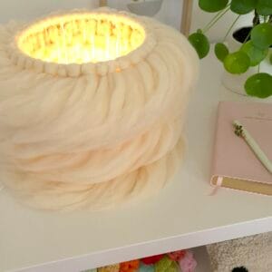 Lontwol lamp op tafel met plant en boekje.