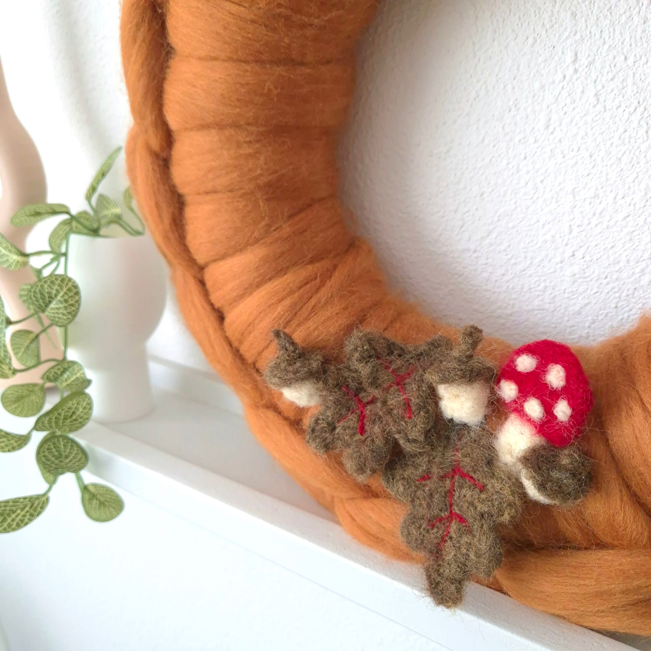 Detail van de herfst krans met geprikvilte paddenstoel, blaadjes en eikeltjes.